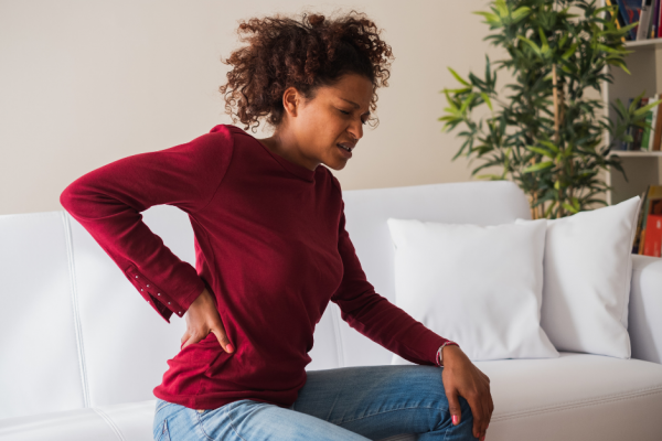 Frau in rotem Pullover hält sich den Rücken wegen Rückenschmerzen